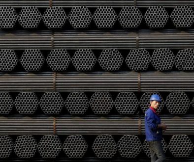 File photo of a worker walking past a pile of steel pipe products at the yard of Youfa steel pipe plant in Tangshan in China's Hebei Province